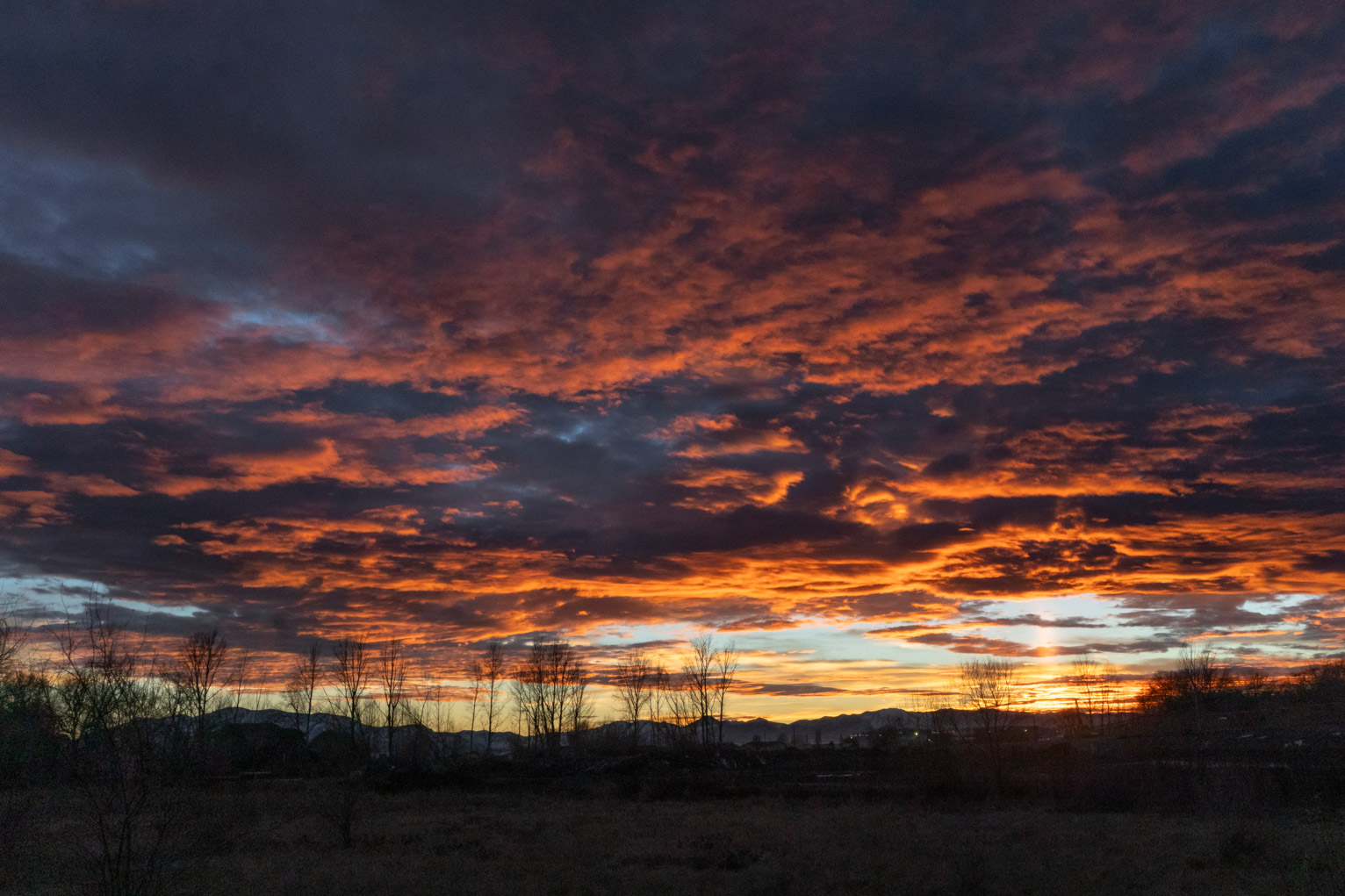 The clouds are lit brilliantly orange, a light pillar is seen where the sun just set